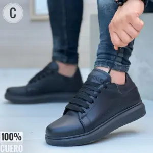 Zapatos deportivos escolares de cuero negro liso. Vista lateral de una persona con jeans ajustando los cordones de este calzado de 100% cuero.